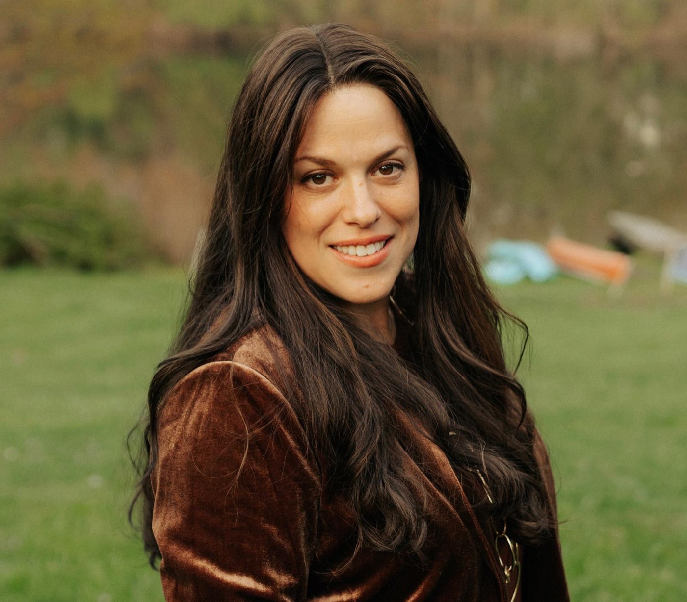 Chanale smiling outdoors in a brown velvet jacket, with green grass and trees behind her